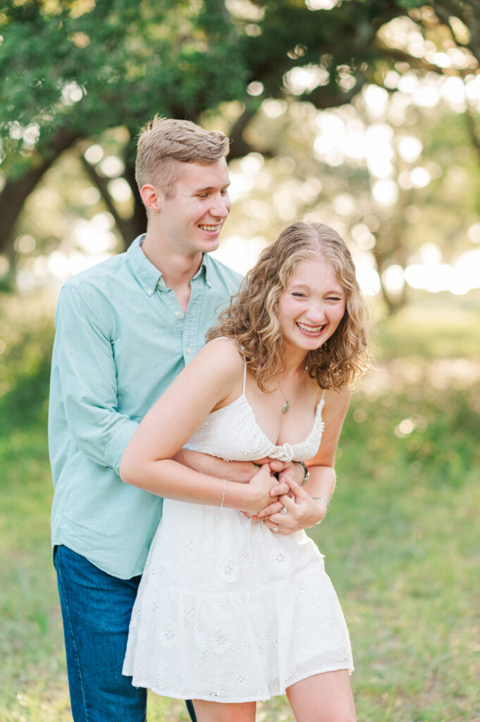 Aubrey laughing as Nolan hugs her from behind during their natural engagement session on Florida's Emerald Coast.