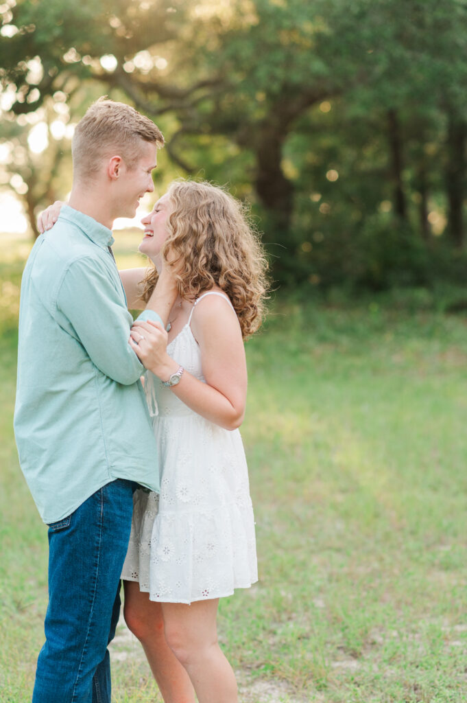 Aubrey and Nolan smiling together during an outdoor engagement session surrounded by oak trees in the Florida Panhandle.