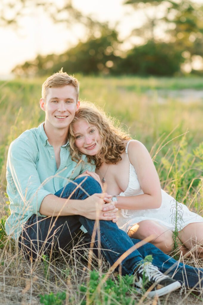 Engaged couple sitting together in a grassy field during sunset engagement photos on Florida's Emerald Coast.