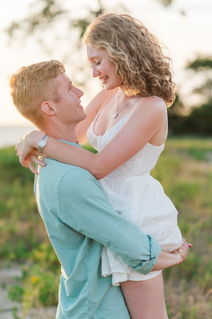 Groom lifting his fiancée during a golden hour engagement session on Florida's Emerald Coast, capturing a joyful and romantic moment.
