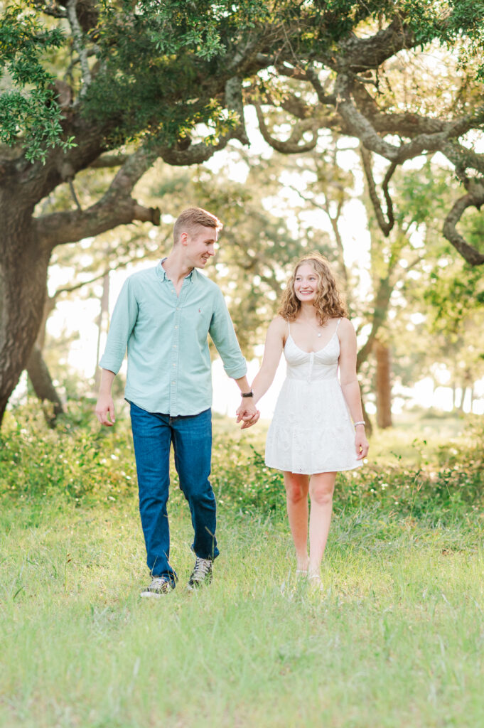 Aubrey and Nolan walking hand in hand beneath historic live oak trees during their Emerald Coast engagement session.