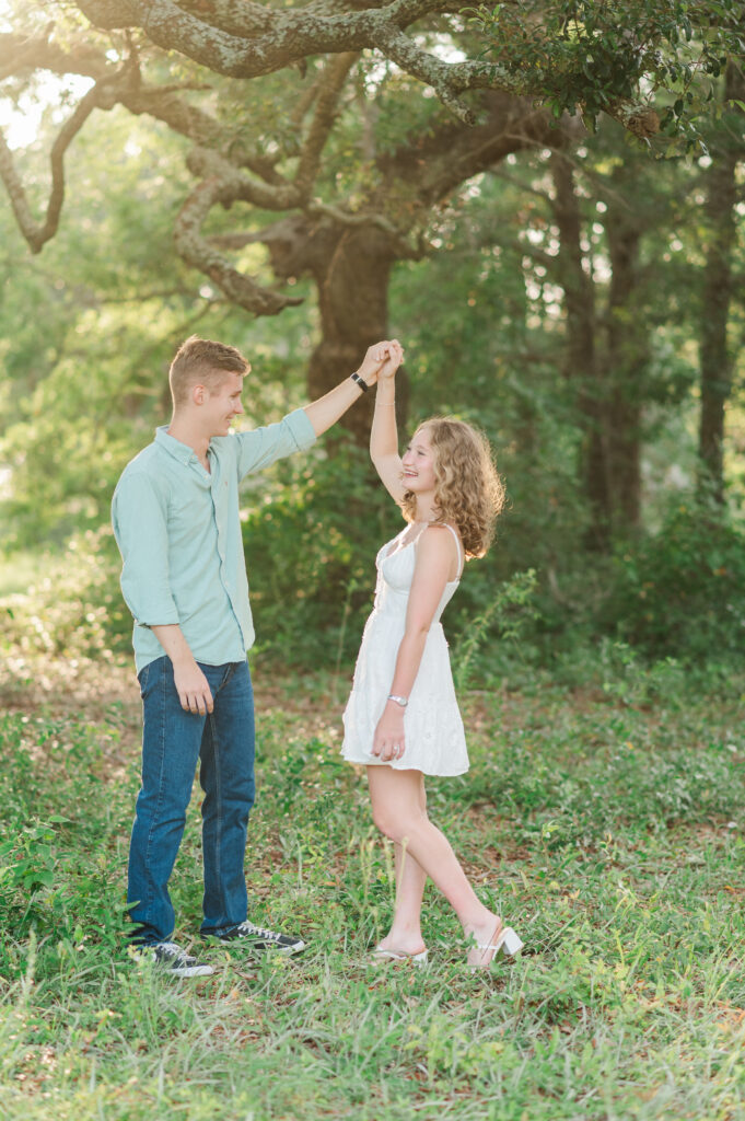 Engaged couple sharing a playful twirl beneath live oak trees during a golden hour engagement session on Florida's Emerald Coast.