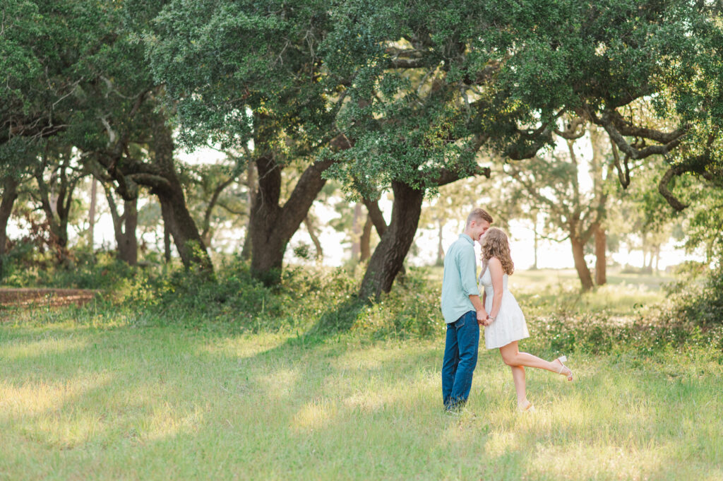 Engaged couple holding hands beneath oak trees during a golden hour engagement session at Turkey Creek Park near Niceville on Florida's Emerald Coast.