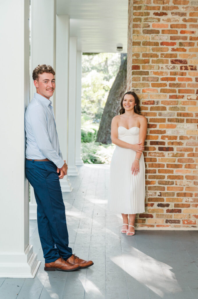Engaged couple smiling together on the wraparound porch of the historic Wesley House at Eden Gardens State Park.