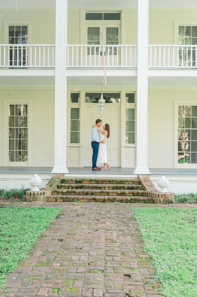 Engaged couple embracing on the front porch of the historic Wesley House at Eden Gardens State Park in Santa Rosa Beach, Florida.