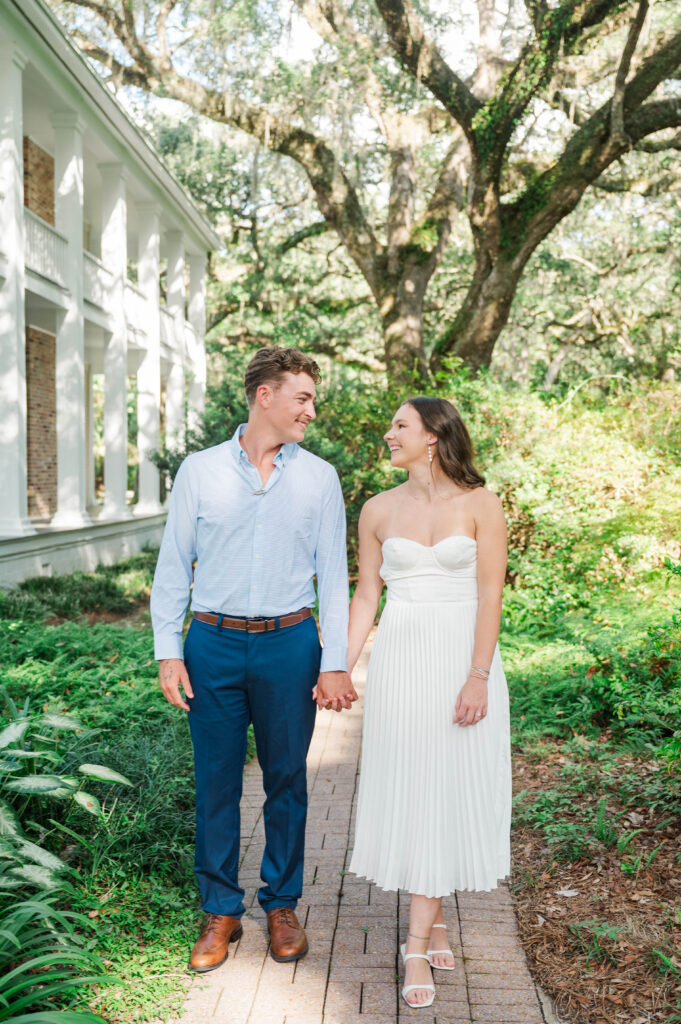 Engaged couple standing together along a lush garden pathway at Eden Gardens State Park in Santa Rosa Beach, Florida.