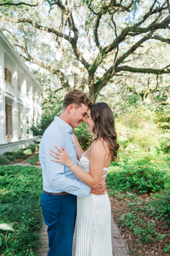 Engaged couple smiling together beneath moss-draped live oaks at Eden Gardens State Park in Santa Rosa Beach, Florida.