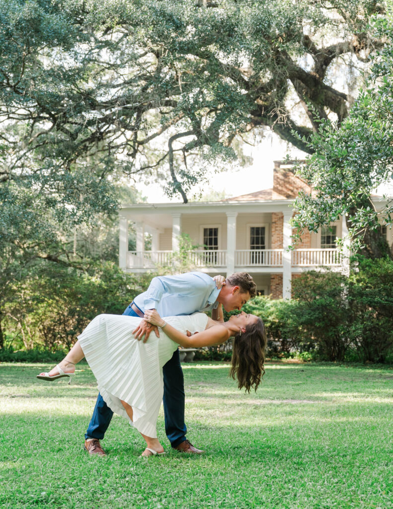 Engaged couple sharing a playful dip and kiss on the lawn in front of the Wesley House at Eden Gardens State Park.