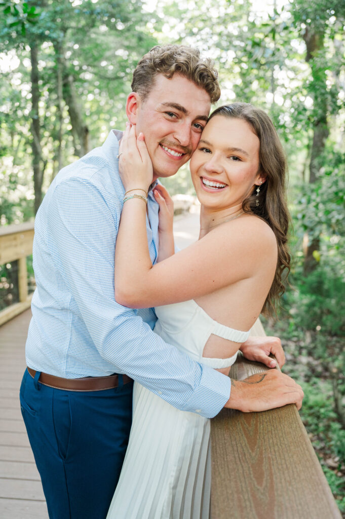 Engaged couple smiling together on a wooden bridge surrounded by greenery at Eden Gardens State Park.