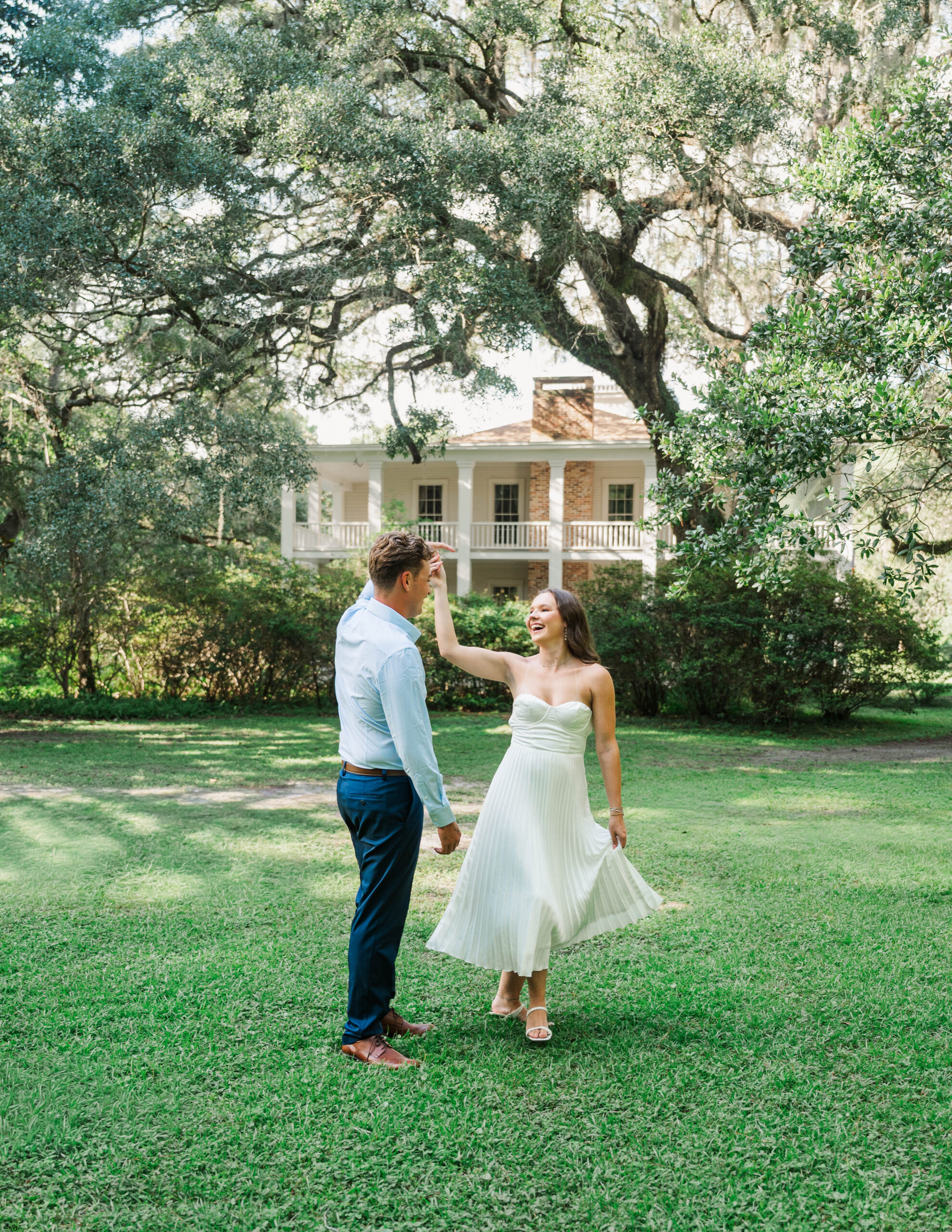 Engaged couple dancing beneath live oaks with the historic Wesley House at Eden Gardens State Park in Santa Rosa Beach, Florida.